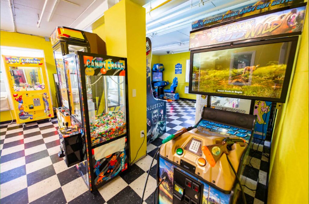 A room with yellow walls and a black and white checkered floor, featuring several arcade machines.