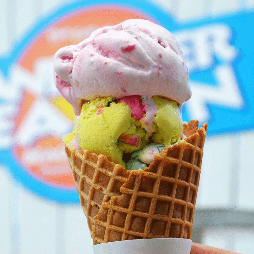 A scoop of yellow ice cream and a scoop of pink ice cream in a waffle cone.
