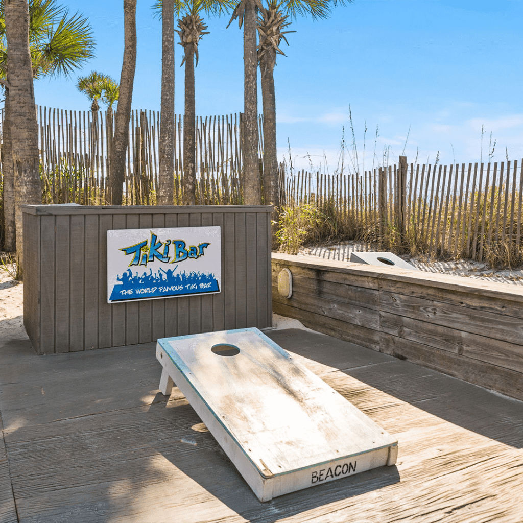 A wooden cornhole game sits on a deck in front of a Tiki Bar sign.